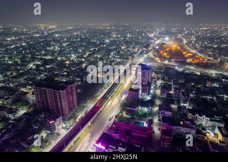 aerial drone shot showing elevated metro track over lit road surrounded by densely populated buildings with homes shops and skyscrapers Stock Photo