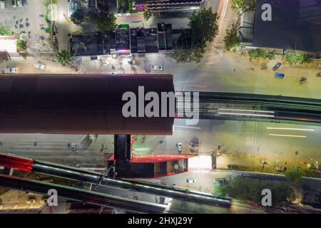 top down aerial drone shot showing metro leaving from red dome roofed elevated metro station over lit road and parking Stock Photo