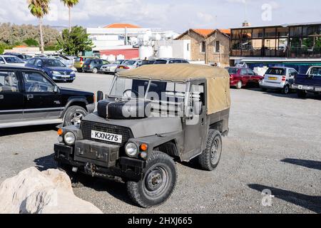 Paphos Cyprus - Oct 29, 2014: Front view of old SUV military colored near the marina of Paphos on Apostolou street with Blue Mare cafe in background Stock Photo