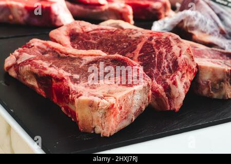 Big chunky raw cuts of beef steaks on a black marble slate Stock Photo