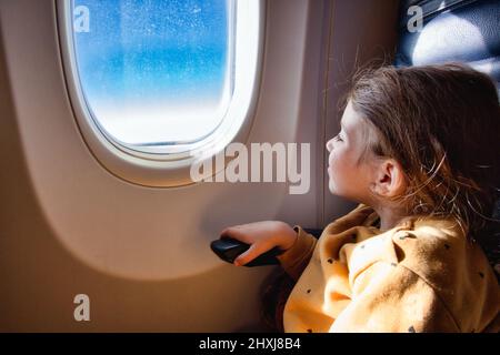 Little girl sat on a commercial flight airplane looking out of the window Stock Photo