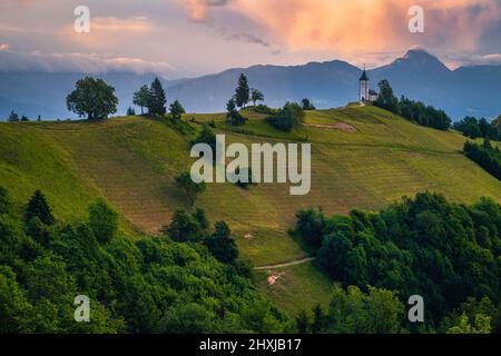 Mountain landscape with church on the mountain ridge. Colorful sunset scenery and famous Saint Primoz church with mountains in background, Jamnik vill Stock Photo