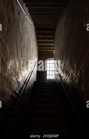 Dark and creepy window open at top of old stone stairs bright sun light rays shining through on floor making shadows and scary sinister abandoned base Stock Photo