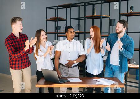 Portrait of happy multiethnic business team of young startup businesspeople laughing joking having fun standing together in modern coworking room. Stock Photo