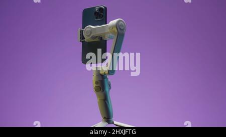Russia - Moscow, 11.25.2021: close up of new smartphone being held in functional tripod. Action. New professional phone with three cameras rotating Stock Photo