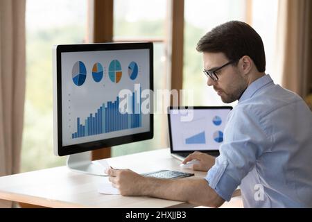Serious young businessman work with infographic on laptop desktop computers Stock Photo