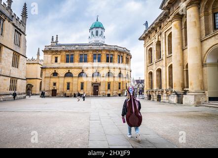 A  young musician  carrying her cello through Bodleian Library courtyard in Oxford, UK.. The Old Bodleian Library (left), Sheldonian Theatre (centre) Stock Photo