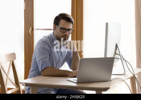 Serious young man work from home office on two computers Stock Photo