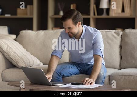 Smiling young businessman pay taxes online from home using laptop Stock Photo