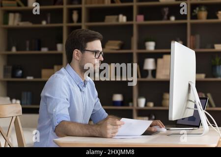 Busy male manager analyze financial documents at workplace using computer Stock Photo