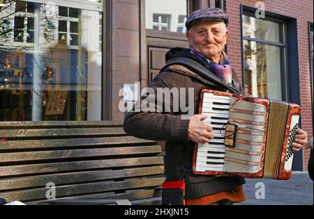 Düsseldorf, Germany - March 9. 2022: Closeup of old standing man with hat playing piano accordion on public street Stock Photo