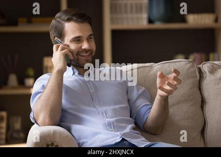 Relaxed millennial guy sitting on sofa having nice telephone conversation Stock Photo