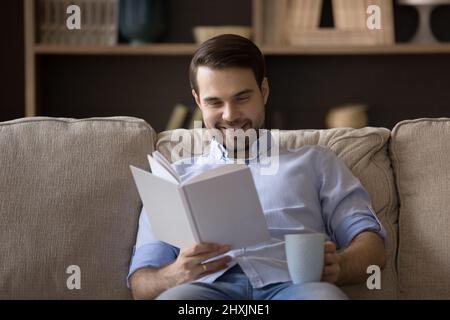 Young man reader holding cup of coffee enjoying favorite book Stock Photo