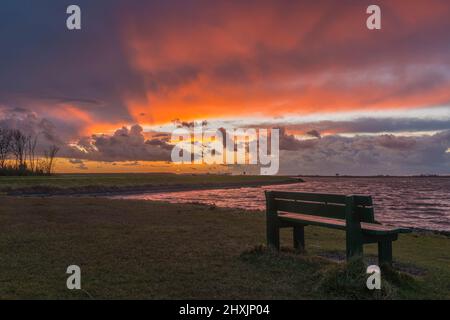 Dramatic thunderstorm clouds approaching a bench on the Veerse Meer at sunset. Zeeland, Netherlands Stock Photo