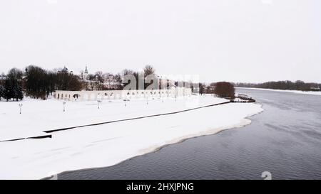 Flying over the winter river partially covered by ice and snow on cloudy sky background. Concept. Cold weather in a small town with bald trees. Stock Photo