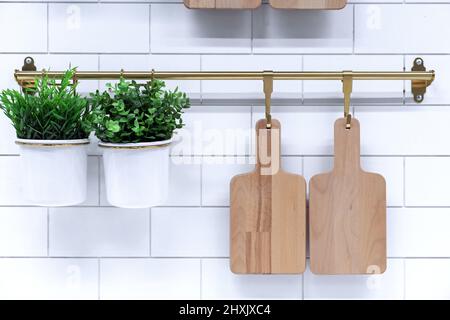 Wooden cutting boards and pots of flowers on the hooks of a kitchen metal rail. Stock Photo