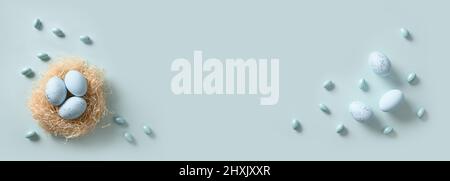 Easter blue eggs in nest on monochrome blue background. Banner. Spring greeting card with copy space. Top view. Minimal flat lay. Stock Photo