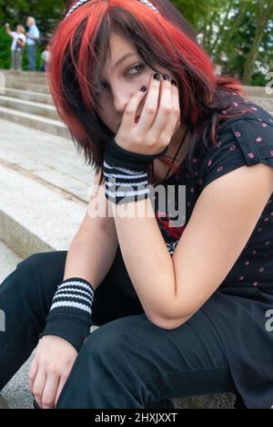 Punk emo girl, young adult with black red hair, sitting on a