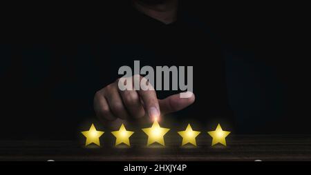 Gold five stars point, best excellent rating satisfaction pointing by the finger of man in black on dark background. Banner for customer service evalu Stock Photo