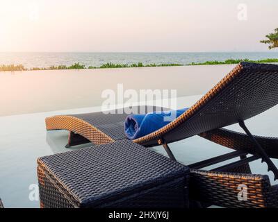 Blue towel pool for the guest rolled on modern rattan sunbed on white marble floor at swimming pool with sea view at the hotel resort, holiday vacatio Stock Photo