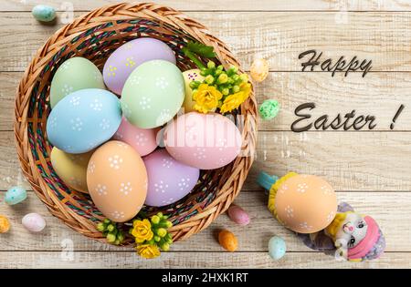 Colored easter eggs in a basket on a rustic wooden table.  Overhead view with Happy Easter text Stock Photo