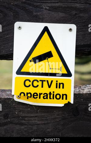 Broken yellow cctv in operation warning sign on a wooden fence Stock Photo