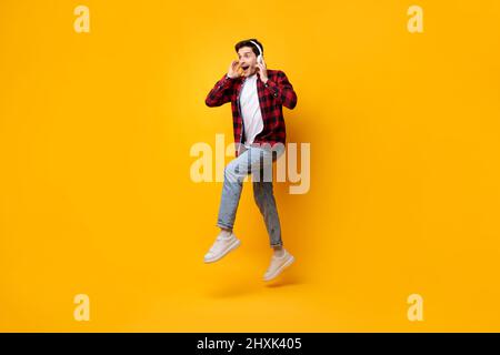 Excited young man in headset jumping up at orange studio Stock Photo