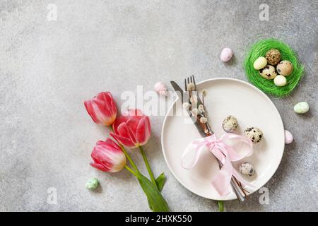 Festive Easter table setting with painted eggs, spring flowers and cutlery on light grey tabletop. Table setting for Happy Easter day.  Top view flat Stock Photo