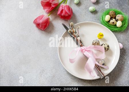 Festive Easter table setting with painted eggs, spring flowers and cutlery on light grey tabletop. Table setting for Happy Easter day.  Copy space. Stock Photo