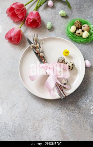Festive Easter table setting with painted eggs, spring flowers and cutlery on light grey tabletop. Table setting for Happy Easter day. Copy space. Stock Photo