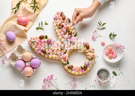 Woman with beautiful cake and painted eggs for Easter celebration on light background Stock Photo