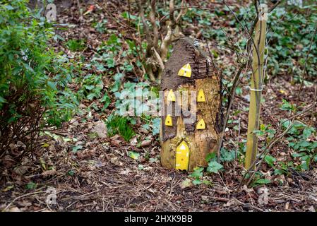 Tall wooden fairy house with yellow windows and fairy door, made from tree stump in Irish woodland fairy garden. Stock Photo