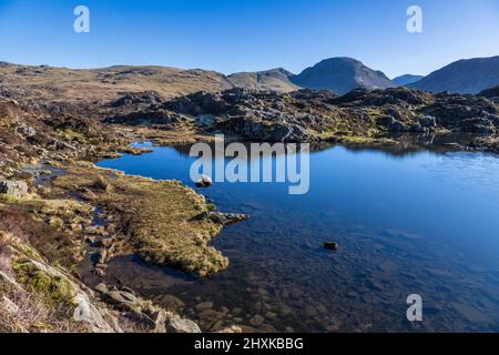 A partially frozen Innominate Tarn with Great Gable and Scar Fell Pike in the background, Lake District, England Stock Photo