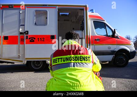 Zeuthen, Germany. 11th Mar, 2022. 'Rescue service' is written on the jacket of a man squatting in front of an ambulance of the Zeuthen fire department. Filming is taking place here for the Sat.1 series 'Lenßen übernimmt' on the subject of 'attacks on emergency services. The episode is broadcast as part of a special week on the topic of 'victim protection. Credit: Jens Kalaene/dpa-Zentralbild/dpa/Alamy Live News Stock Photo