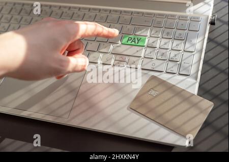 Online payment concpet. Hand, finger pressing green safe PAY key, button on laptop keyboard. Stock Photo
