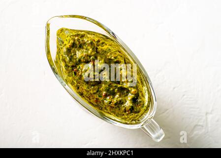 Chimichurri sauce in a gravy bowl on a white background. Argentinean vegetarian sauce made from olive oil, oregano, parsley. Stock Photo