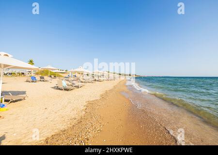 Beautiful view of empty sandy beach with white umbrellas and sun loungers against blue sky. Greece. Stock Photo