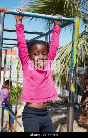 Holding on tight to carefree days of youth. Portrait of a happy little girl hanging on a jungle gym. Stock Photo