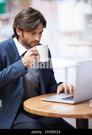 Some casual browsing during my lunch hour. A handsome businessman working on his laptop and drinking coffee at a coffeeshop. Stock Photo