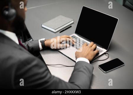 Unrecognizable black businessman using laptop with empty screen and headset Stock Photo