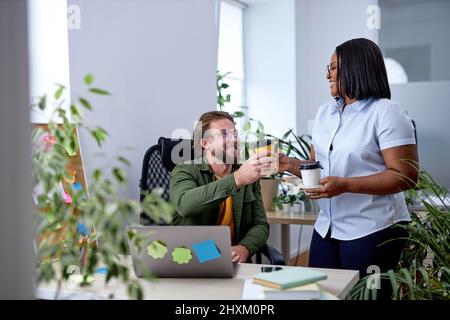 Attractive Black Female Manager Talking To Colleague Employee, Having Break Time With Coffee. In Office. Young Black Lady Mentor Coach Talking to Male Stock Photo