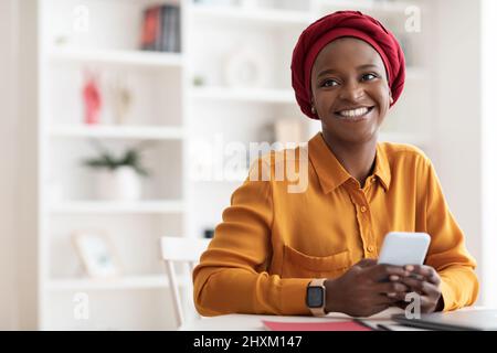 Positive muslim black woman using mobile phone and smiling Stock Photo