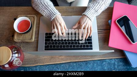 Woman working on a laptop in a cafe with a cup of tea, top view. Stock Photo
