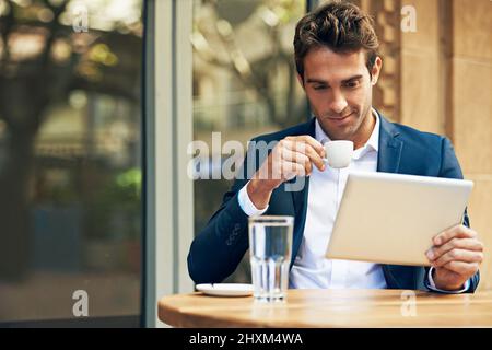 His favorite place for coffee and wifi. A young businessman using his digital tablet while having coffee at an outdoor cafe. Stock Photo