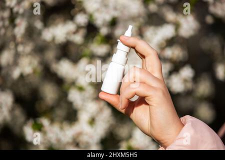 Allergy concept, young woman with nose or nasal spray in hand in front of blooming a tree during spring season, healthcare Stock Photo