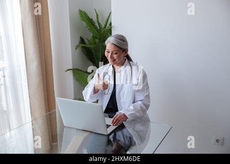 Doctor woman working from home, communicating via video using laptop Stock Photo