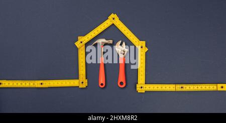 Home repair. Hand tools under house shape yellow wooden measure, blue background. Folding ruler and hardware, workshop, construction, renovation conce Stock Photo