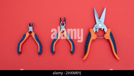 Sheet metal shears with steel point, orange, blue color rubber handle on red background. Three hand tool various size, new pincer, scissors, with shar Stock Photo
