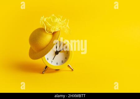 Daylight saving time. Spring forward. Alarm clock with hat on yellow background Stock Photo
