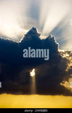 SUN RAYS BREAKING THROUGH LARGE STORM CLOUD WITH YELLOW GLOW Stock Photo